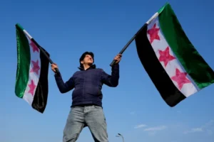 A Syrian man waves the Syrian “revolutionary” flags, as he continues to celebrate the ousting of Bashar al-Assad’s government, at Umayyad Square, in Damascus, Syria, Friday, Dec. 20, 2024. (AP Photo/Hussein Malla)